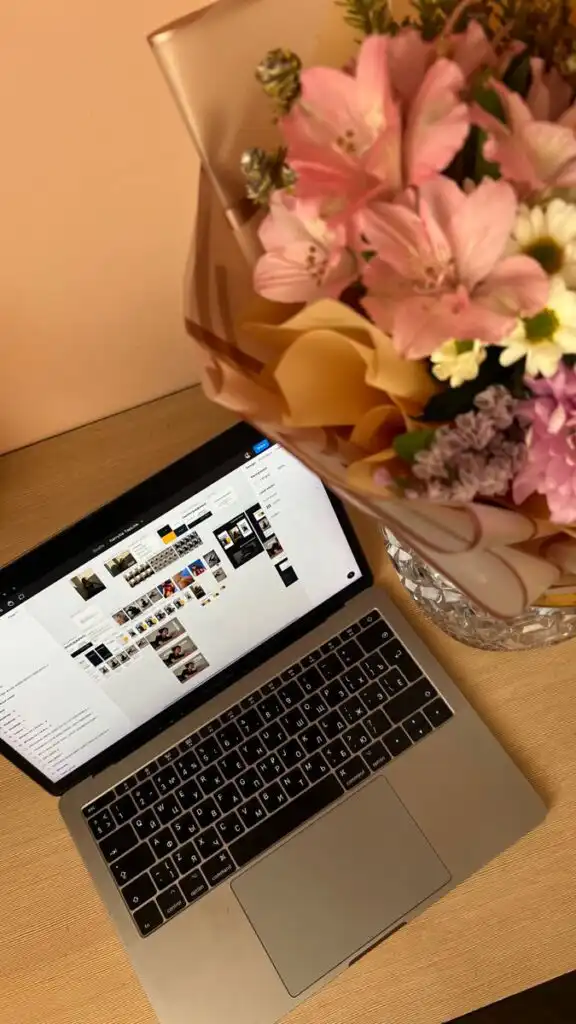 Laptop with open screen on desk beside a vibrant bouquet of pink and white flowers. Ideal workspace setting.