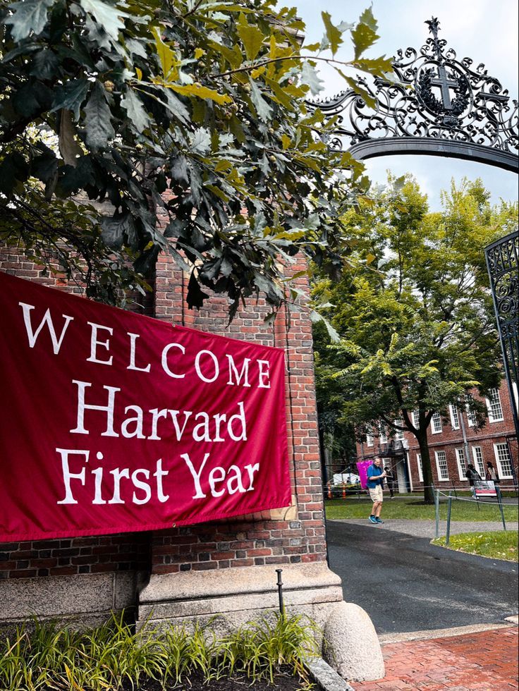 a7b72487-39df-44e8-9a21-83e112d290bc Harvard University welcomes first-year students with a red banner in front of a historic brick gate, lush greenery nearby. | Sky Rye Design Harvard University welcomes first-year students with a red banner in front of a historic brick gate, lush greenery nearby.