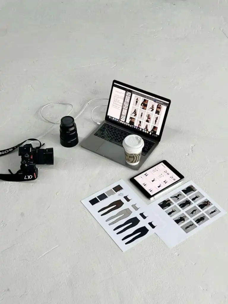 ae43f421bd83c4d966b9f60b873d7bd2 Photography setup with a laptop, tablet, camera, and coffee on a studio floor, featuring model photos and clothing designs. | Sky Rye Design Photography setup with a laptop, tablet, camera, and coffee on a studio floor, featuring model photos and clothing designs.