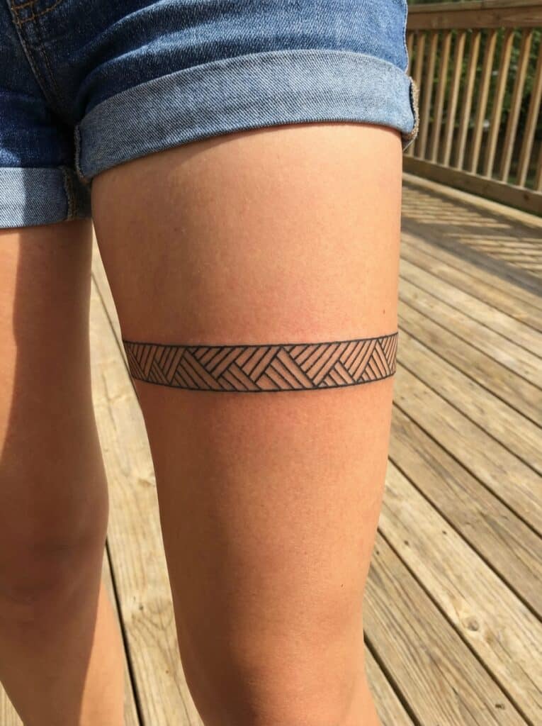 ai-photo-studio-1765816865398-1 Geometric band tattoo on upper thigh, featuring interlocking patterns, with denim shorts and wooden deck background under sunlight. | Sky Rye Design Geometric band tattoo on upper thigh, featuring interlocking patterns, with denim shorts and wooden deck background under sunlight.