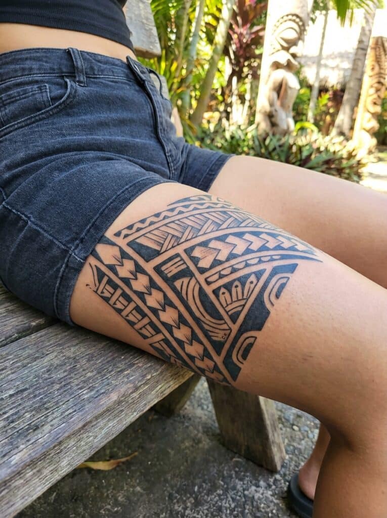 ai-photo-studio-1765905443051-1 Close-up of a tribal tattoo on a person's thigh, sitting outdoors on a wooden bench in shorts. | Sky Rye Design Close-up of a tribal tattoo on a person's thigh, sitting outdoors on a wooden bench in shorts.
