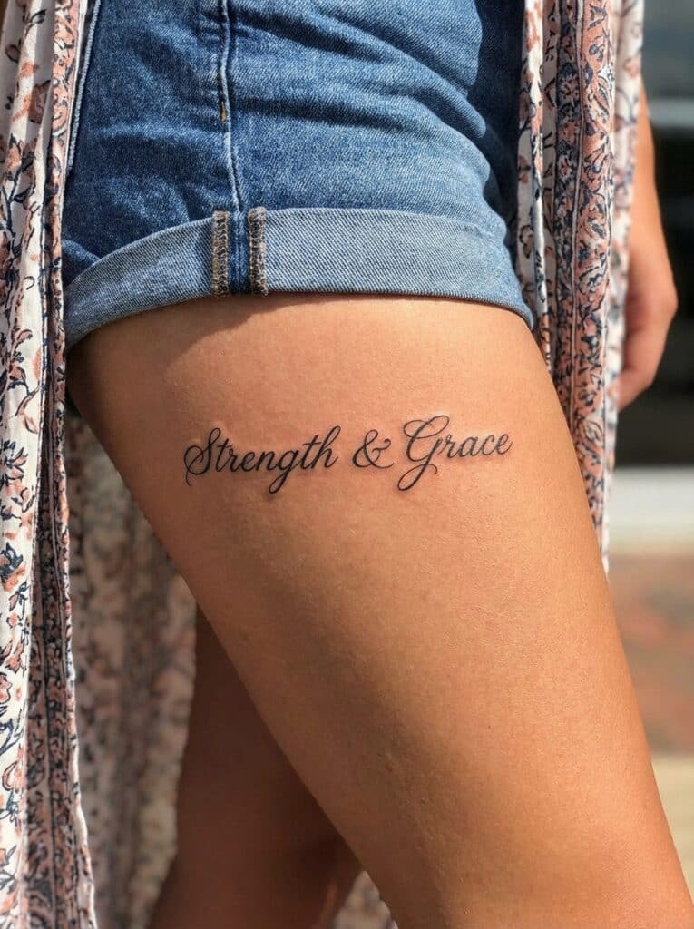 ai-photo-studio-1765905865365-2 Close-up of thigh tattoo with the words Strength & Grace in elegant script. Tattoo is below denim shorts, adorned with floral shawl. | Sky Rye Design Close-up of thigh tattoo with the words Strength & Grace in elegant script. Tattoo is below denim shorts, adorned with floral shawl.