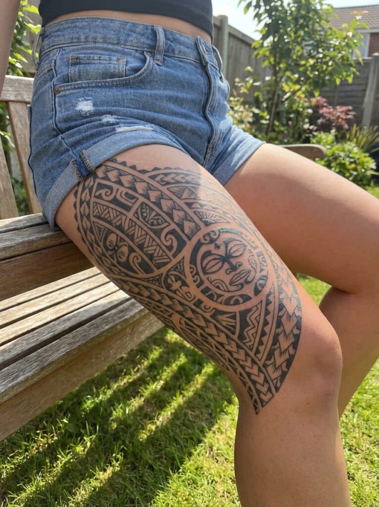 ai-photo-studio-1765997866322-1 Intricate tribal-style tattoo on a woman's thigh in denim shorts, sitting on a wooden bench in a sunny garden. | Sky Rye Design Intricate tribal-style tattoo on a woman's thigh in denim shorts, sitting on a wooden bench in a sunny garden.