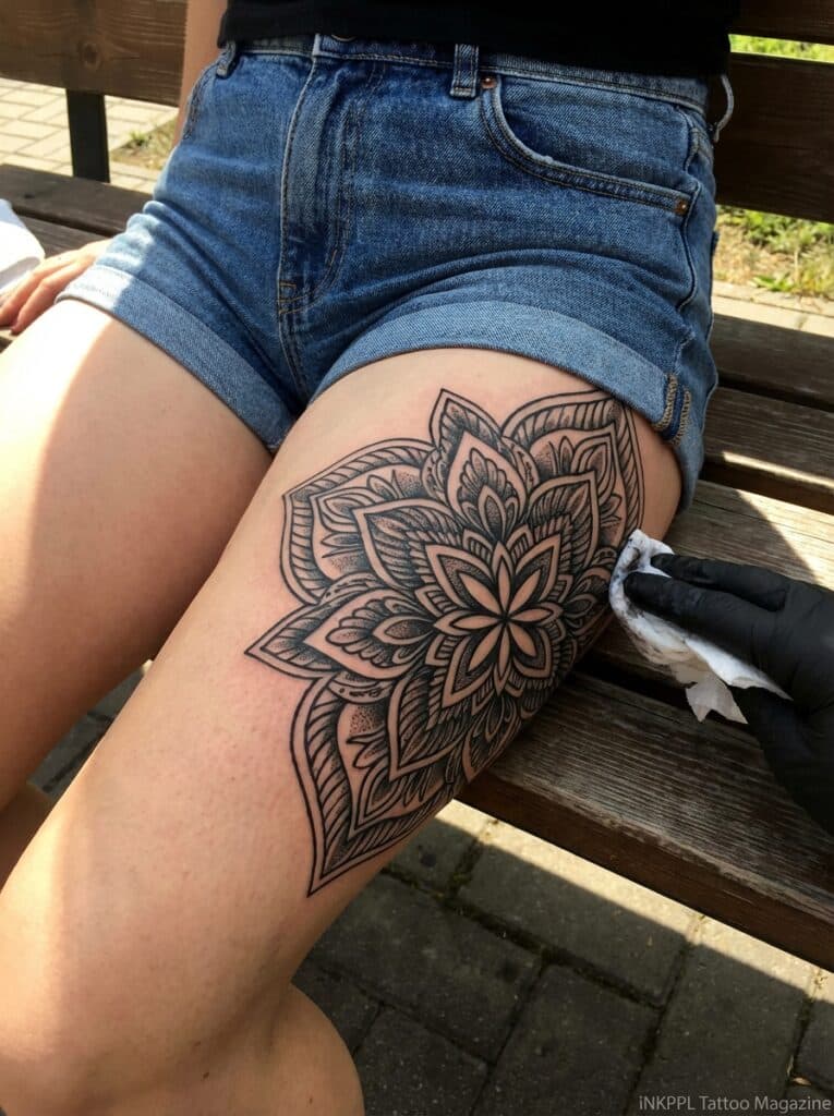 ai-photo-studio-1765998390926-2 Person with a detailed floral thigh tattoo wearing denim shorts, while a gloved hand cleans the design. | Sky Rye Design Person with a detailed floral thigh tattoo wearing denim shorts, while a gloved hand cleans the design.