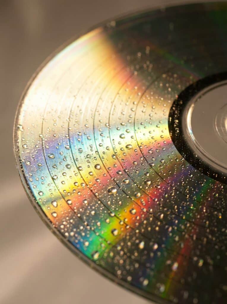 ai-photo-studio-1766413683180-1 Close-up of a CD with rainbow reflections and water droplets, capturing a vibrant, colorful spectrum on its shiny surface. | Sky Rye Design Close-up of a CD with rainbow reflections and water droplets, capturing a vibrant, colorful spectrum on its shiny surface.