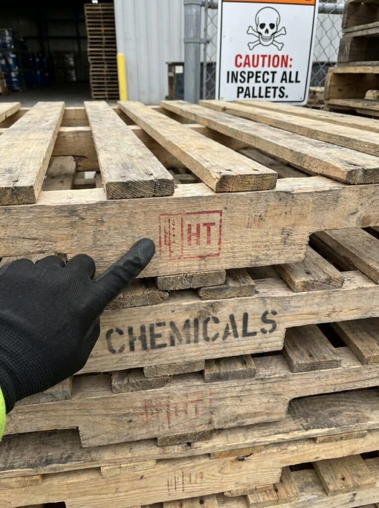 ai-photo-studio-1766516844192-1 Gloved hand points to heat-treated wooden pallet marked for chemical use, highlighting safety sign: Inspect All Pallets. | Sky Rye Design Gloved hand points to heat-treated wooden pallet marked for chemical use, highlighting safety sign: Inspect All Pallets.