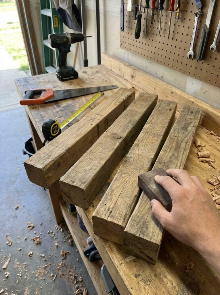 ai-photo-studio-1766673648085-1 Hand sanding wooden planks in a workshop, surrounded by tools like a saw, drill, and measuring tape on the workbench. | Sky Rye Design Hand sanding wooden planks in a workshop, surrounded by tools like a saw, drill, and measuring tape on the workbench.