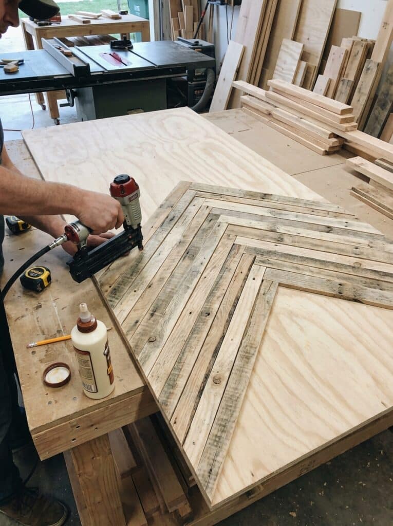 ai-photo-studio-1766673931965-1 Woodworker using a nail gun to create a geometric wooden pattern on a large plywood board in a carpentry workshop. | Sky Rye Design Woodworker using a nail gun to create a geometric wooden pattern on a large plywood board in a carpentry workshop.