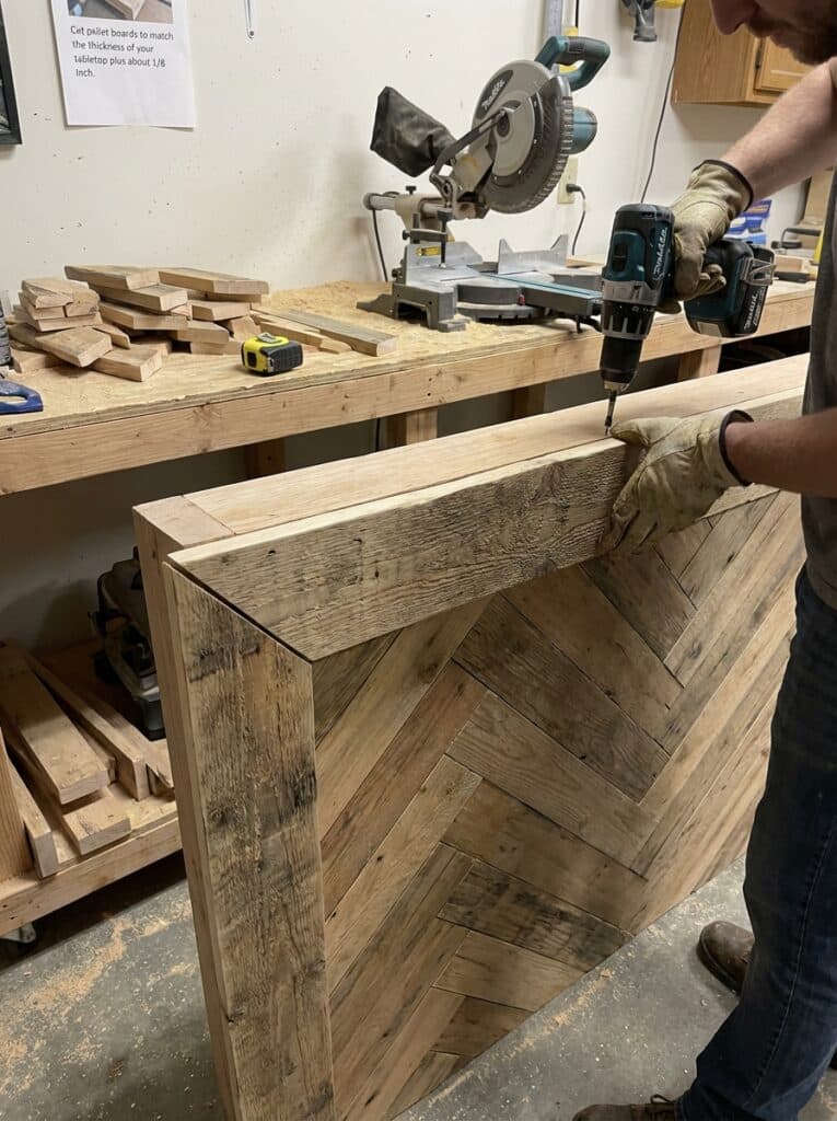 ai-photo-studio-1766673986655-2 Carpenter using a power drill to assemble a wooden herringbone table in a workshop with tools and materials on the workbench. | Sky Rye Design Carpenter using a power drill to assemble a wooden herringbone table in a workshop with tools and materials on the workbench.