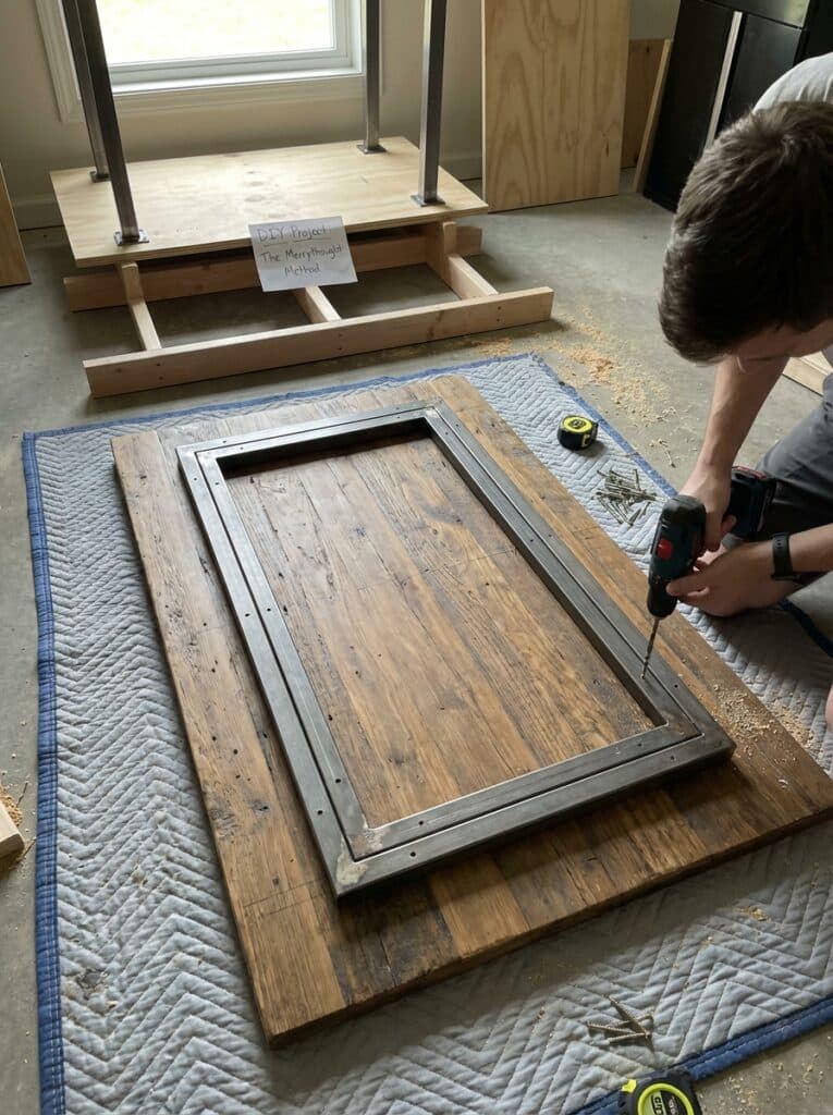 ai-photo-studio-1766674115128-2 Man drills frame for DIY table project on quilted mat with tools nearby. | Sky Rye Design Man drills frame for DIY table project on quilted mat with tools nearby.