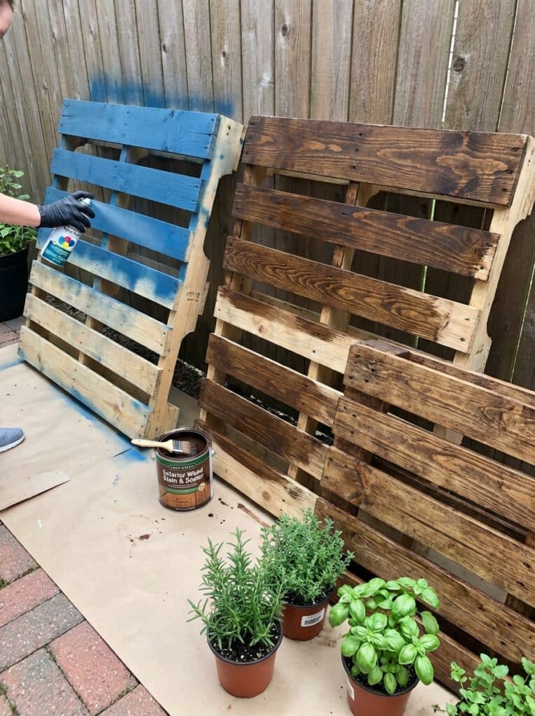 ai-photo-studio-1766676514472-2 Blue and brown wooden pallets being painted in a garden with herbs. DIY outdoor decor project with paint and plants. | Sky Rye Design Blue and brown wooden pallets being painted in a garden with herbs. DIY outdoor decor project with paint and plants.