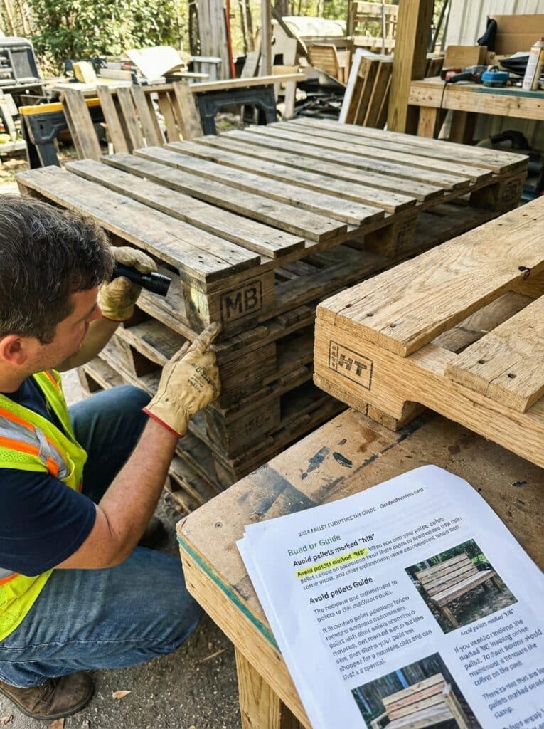 ai-photo-studio-1766940370343-1 Man inspecting wooden pallets in a workshop, pointing at markings for safety and quality control. Safety guide visible on table. | Sky Rye Design Man inspecting wooden pallets in a workshop, pointing at markings for safety and quality control. Safety guide visible on table.