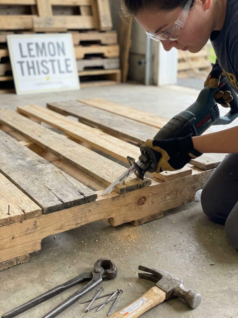ai-photo-studio-1766940511088-2 Person using a Bosch saw to cut wood pallet, with tools and nails on the ground. DIY woodworking project in a workshop setting. | Sky Rye Design Person using a Bosch saw to cut wood pallet, with tools and nails on the ground. DIY woodworking project in a workshop setting.