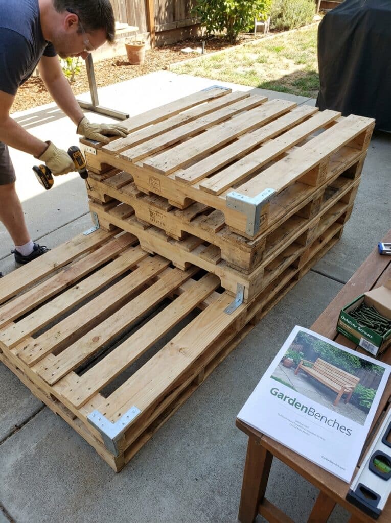 ai-photo-studio-1766940992209-1 Man building a garden bench using wooden pallets and power tools, with instruction booklet on a nearby table outdoors. | Sky Rye Design Man building a garden bench using wooden pallets and power tools, with instruction booklet on a nearby table outdoors.