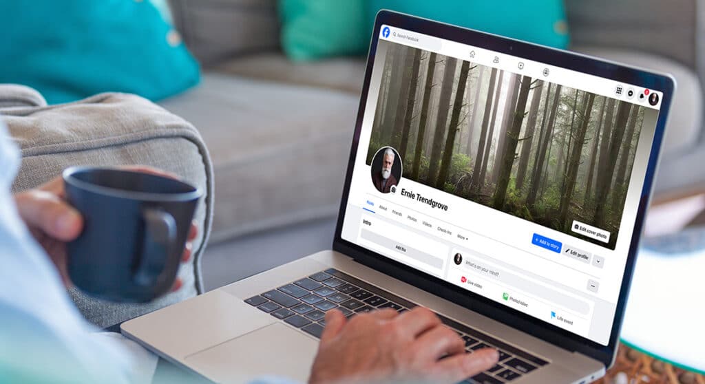 article_deleting_FB Person with a coffee cup browsing Facebook on a laptop, featuring a forest-themed cover photo, seated on a cozy couch. | Sky Rye Design Person with a coffee cup browsing Facebook on a laptop, featuring a forest-themed cover photo, seated on a cozy couch.
