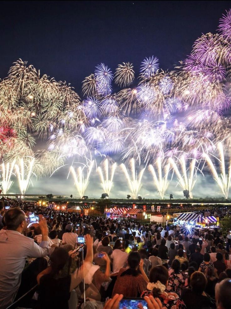 Crowd enjoying a vibrant fireworks display at night, capturing the moment with phones at a bustling outdoor festival.