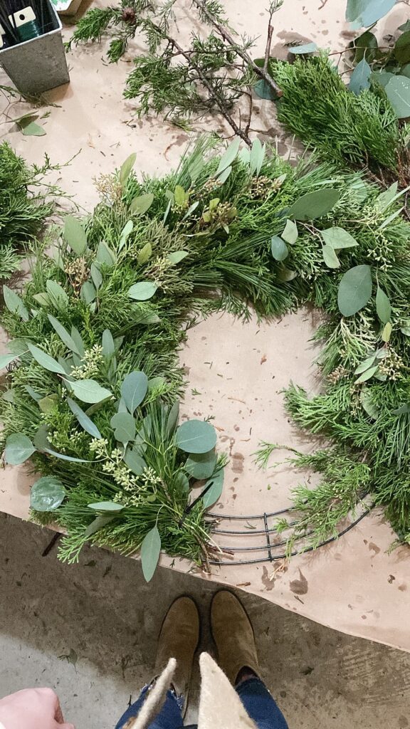 b99680b9ac0509301a91360157314eff Handcrafted green wreath with eucalyptus leaves and pine branches on a table, viewed from above with shoes in the frame. | Sky Rye Design Handcrafted green wreath with eucalyptus leaves and pine branches on a table, viewed from above with shoes in the frame.