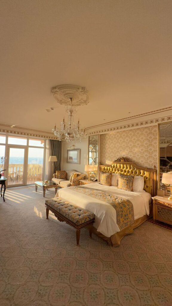 be81630d-f940-4d3f-99ae-014ac49d32c1 Luxurious hotel room featuring elegant decor, a king-sized bed, chandelier, and ocean view windows for a relaxing stay. | Sky Rye Design Luxurious hotel room featuring elegant decor, a king-sized bed, chandelier, and ocean view windows for a relaxing stay.