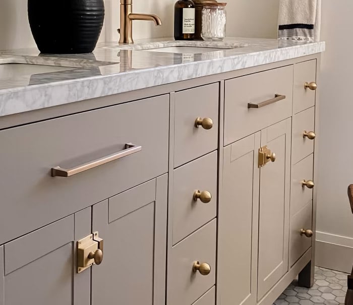 Modern bathroom vanity with gray cabinets, gold hardware, and a marble countertop. Features elegant fixtures and contemporary decor.
