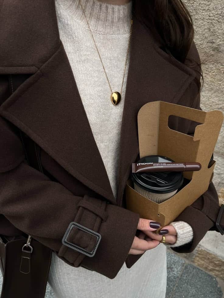 brown🧺🤎🍂 Woman in stylish brown coat holding coffee and a takeaway tray, wearing a cream sweater and gold pendant necklace. Cozy autumn fashion. | Sky Rye Design Woman in stylish brown coat holding coffee and a takeaway tray, wearing a cream sweater and gold pendant necklace. Cozy autumn fashion.
