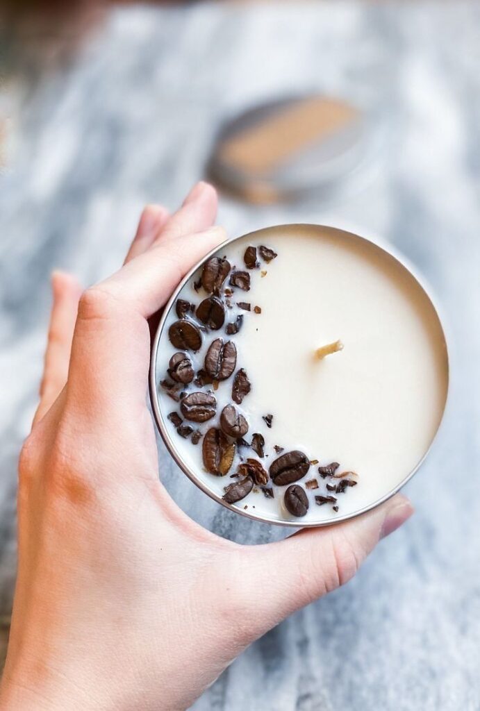 Hand holding a soy candle with embedded coffee beans on a marble surface, creating a cozy, aromatic ambiance.