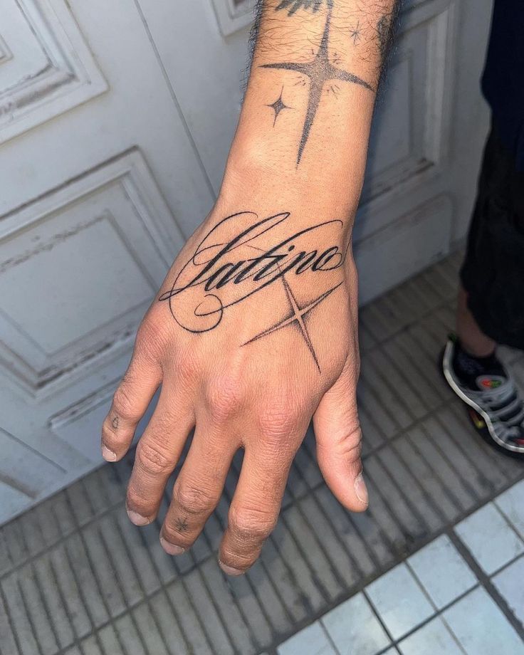 c5fe8ca5-ba0d-4c6b-98b2-ad76009d8f72 Hand tattoo with the word Latino and star designs, showcasing intricate script and creativity on a tiled floor background. | Sky Rye Design Hand tattoo with the word Latino and star designs, showcasing intricate script and creativity on a tiled floor background.