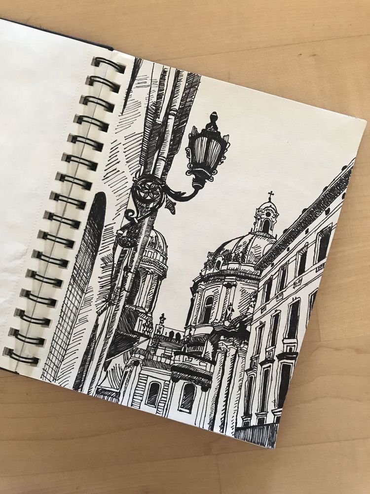 Black ink sketch of a European cathedral in a spiral-bound notebook, featuring ornate architecture and a street lamp.