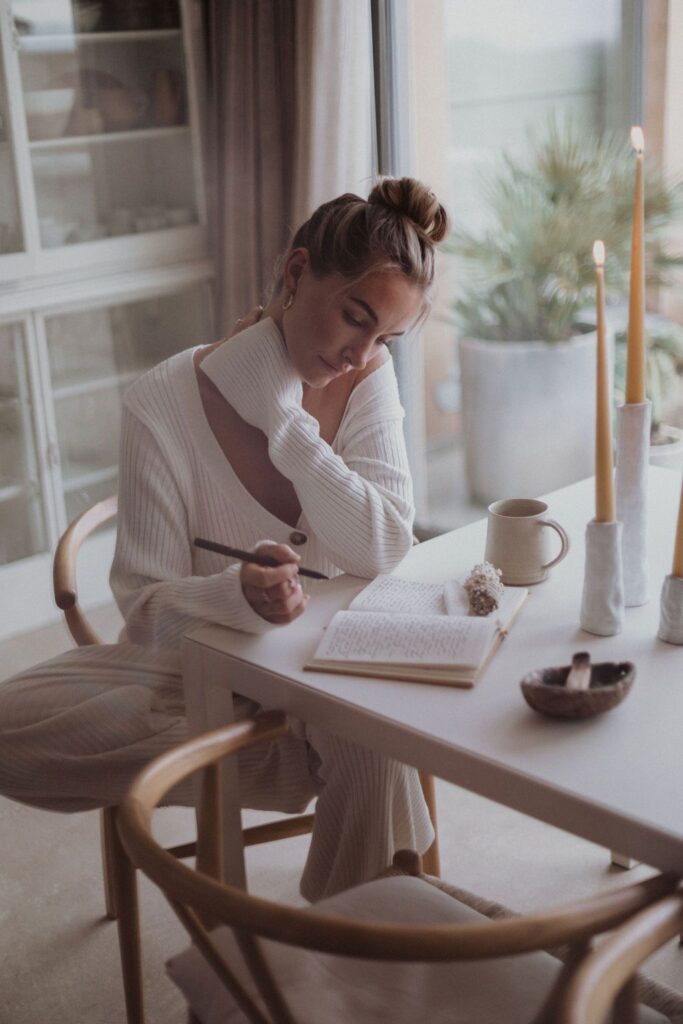 Cozy ambiance with a woman writing in a journal by candlelight, seated at a table with a warm drink, reflecting serene creativity.