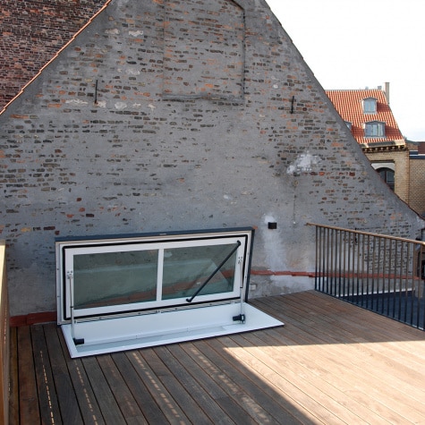 Modern roof access hatch on wooden terrace against rustic brick wall, providing stylish rooftop entry with urban architectural appeal.