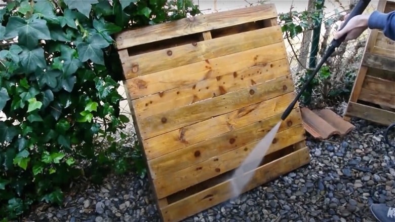 choose-your-pallet-cleaning-method-and-materials-1722006447 Power washing a wooden pallet outdoors, surrounded by greenery and stones, for cleaning and maintenance. | Sky Rye Design Power washing a wooden pallet outdoors, surrounded by greenery and stones, for cleaning and maintenance.
