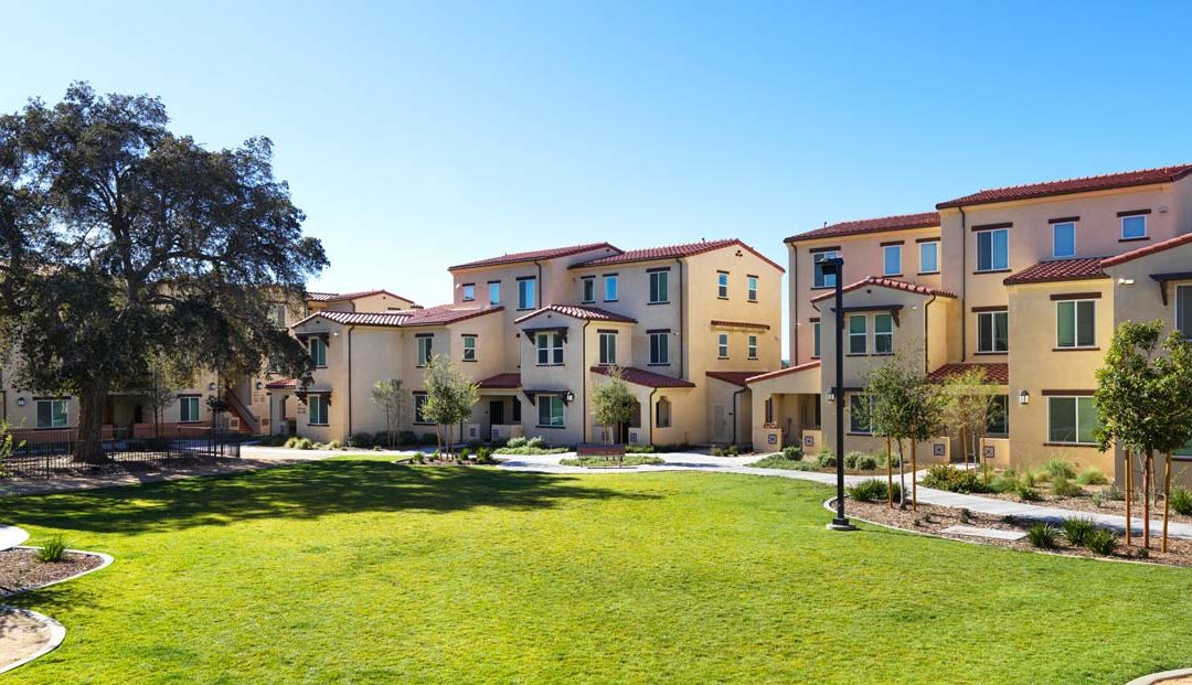Modern apartment complex with green courtyard, blue sky, and trees, highlighting suburban living and community design.