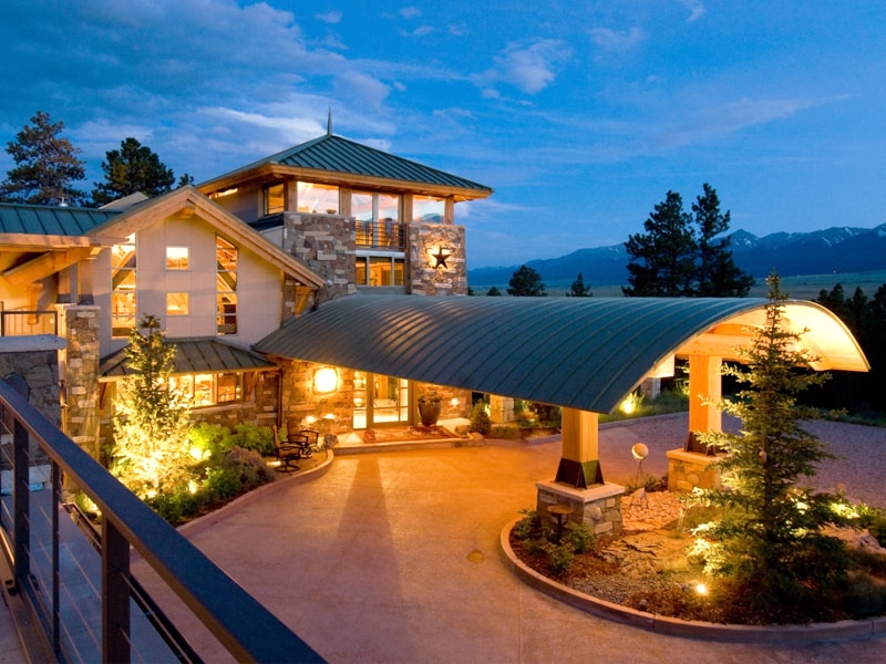 custom Modern mountain lodge with stone facade, large windows, and arched entrance at twilight, surrounded by pine trees and scenic views. | Sky Rye Design Modern mountain lodge with stone facade, large windows, and arched entrance at twilight, surrounded by pine trees and scenic views.