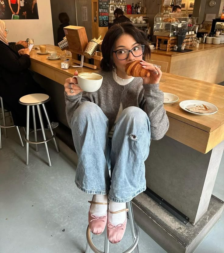 cute coffee photo inspo Young woman enjoying a coffee and croissant at a cafe counter, wearing glasses and casual attire, creating a cozy vibe. | Sky Rye Design Young woman enjoying a coffee and croissant at a cafe counter, wearing glasses and casual attire, creating a cozy vibe.