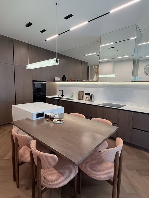 d0de96aaafef70f1b71cd9128655f6f3 Modern kitchen with wooden cabinets, sleek dining table, and pink chairs. Features minimalist decor, hanging light, and mirrored backsplash. | Sky Rye Design Modern kitchen with wooden cabinets, sleek dining table, and pink chairs. Features minimalist decor, hanging light, and mirrored backsplash.