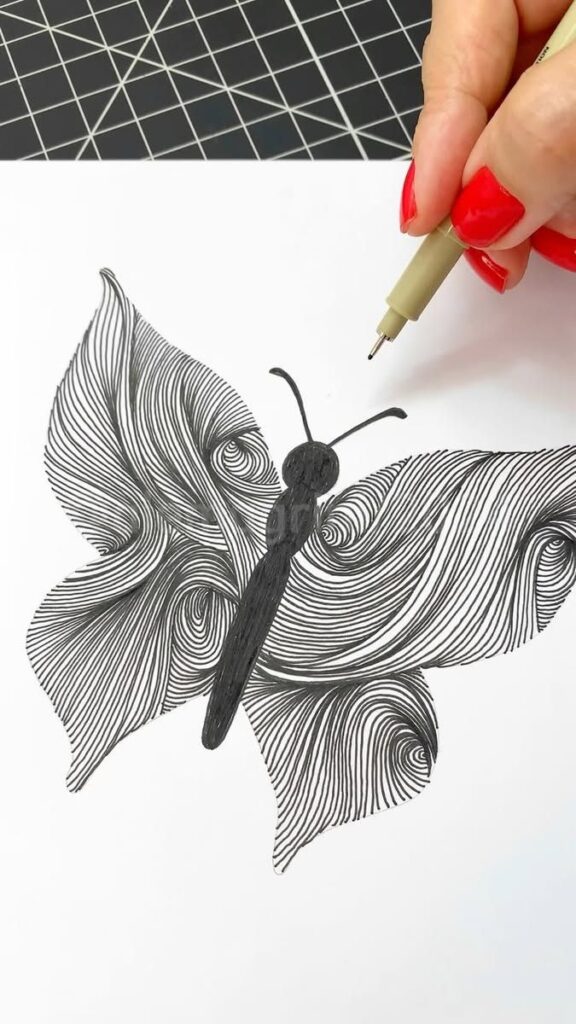 Hand drawing a detailed butterfly with intricate line patterns on wings using a black pen on white paper.