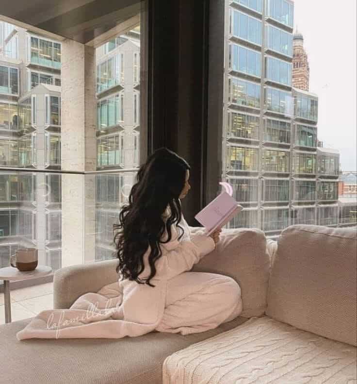 d962ef90-441c-4182-a5bb-387211f4b460 Woman lounging in cozy attire, reading a book by a large window with a cityscape view. Relaxation and urban tranquility. | Sky Rye Design Woman lounging in cozy attire, reading a book by a large window with a cityscape view. Relaxation and urban tranquility.
