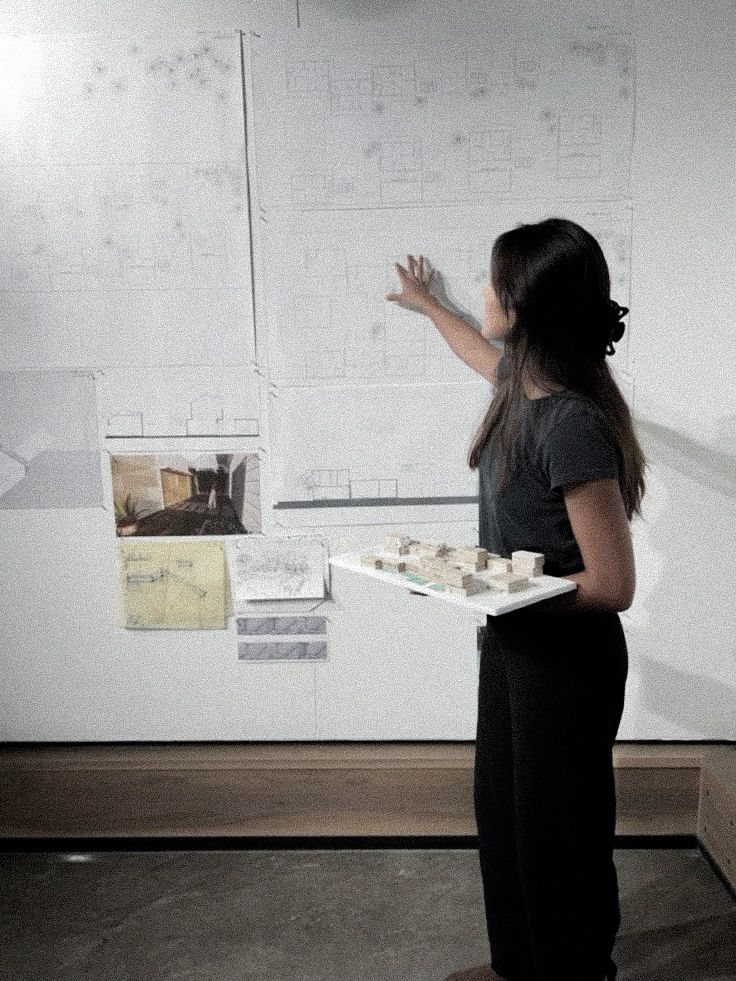 dahlia muñoz _ love redesigned _ lauren asher Architect presents building plans, pointing at designs on a wall, while holding a model. Creative workspace and architectural ideas. | Sky Rye Design Architect presents building plans, pointing at designs on a wall, while holding a model. Creative workspace and architectural ideas.