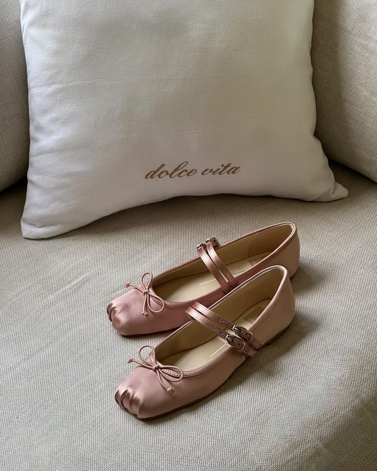 details that dont ask for attention but get it anyway Pink satin ballet flats with bows on a beige couch, next to a dolce vita pillow, creating a cozy and stylish setting. | Sky Rye Design Pink satin ballet flats with bows on a beige couch, next to a dolce vita pillow, creating a cozy and stylish setting.