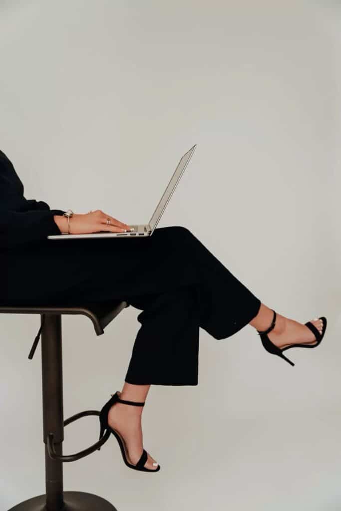 e5be3f8cbd7b66d0e9e0c6a7960ea94d Person seated at a high stool, wearing black attire and heels, using a laptop in a minimalist setting. | Sky Rye Design Person seated at a high stool, wearing black attire and heels, using a laptop in a minimalist setting.