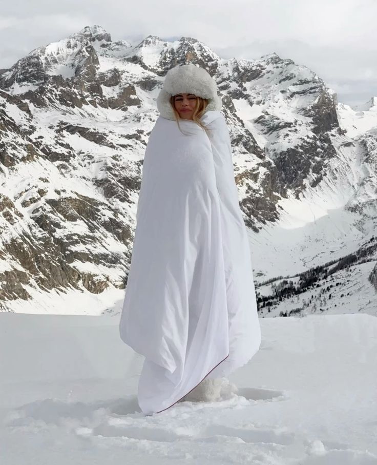 elinwarn Person wrapped in a white blanket on snowy mountain, wearing a fluffy hat. Scenic winter landscape with rugged peaks in the background. | Sky Rye Design Person wrapped in a white blanket on snowy mountain, wearing a fluffy hat. Scenic winter landscape with rugged peaks in the background.