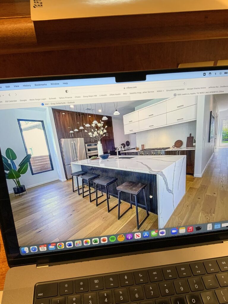 Modern kitchen with marble island, sleek appliances, and bar stools, displayed on a laptop screen, showcasing Zillow website.