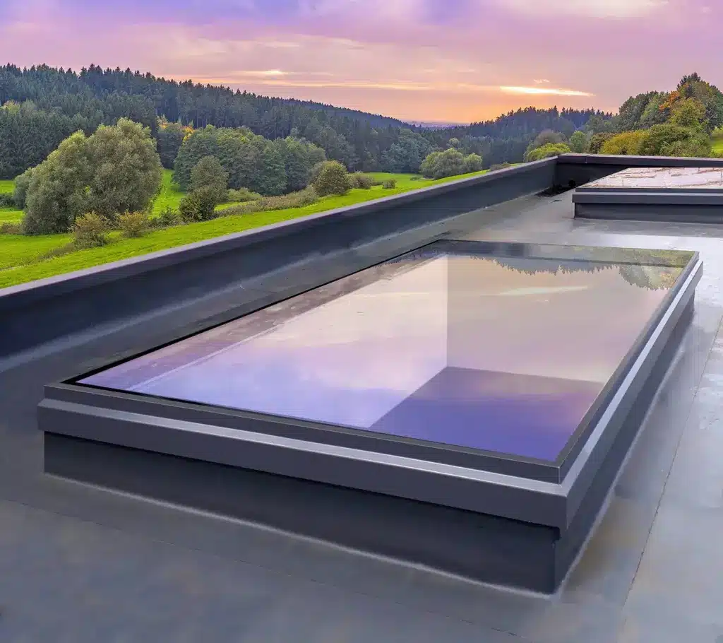 flat-roof-light Modern skylight on a flat roof reflecting the colorful sunset sky and green landscape, blending architecture with scenic beauty. | Sky Rye Design Modern skylight on a flat roof reflecting the colorful sunset sky and green landscape, blending architecture with scenic beauty.