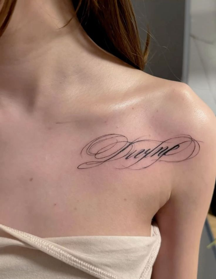 font cursive tattoo _ divine calligraphic tattoo Elegant script tattoo on shoulder, highlighting intricate cursive design on skin. Minimalistic, stylish personal ink art. | Sky Rye Design Elegant script tattoo on shoulder, highlighting intricate cursive design on skin. Minimalistic, stylish personal ink art.
