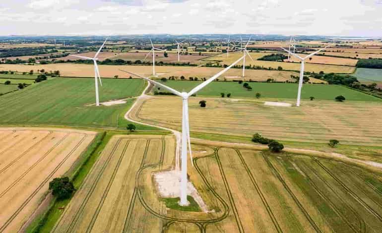 Aerial view of wind turbines on farmland under a cloudy sky, showcasing renewable energy and sustainable agriculture.