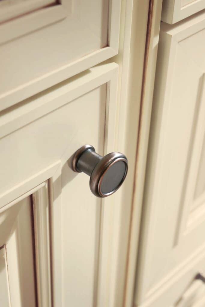 Close-up of a vintage-style cabinet knob on a cream-colored wooden cabinet door.