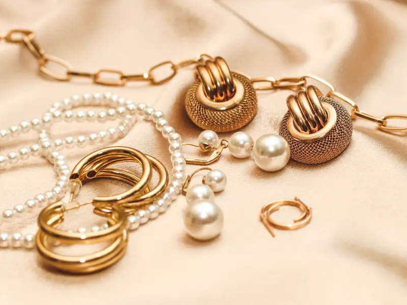 gold-vermeil-jewelry-3 Elegant gold and pearl jewelry set on a beige satin fabric backdrop, showcasing luxury accessories in a sophisticated arrangement. | Sky Rye Design Elegant gold and pearl jewelry set on a beige satin fabric backdrop, showcasing luxury accessories in a sophisticated arrangement.