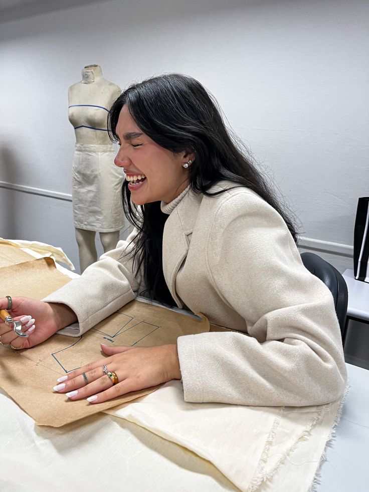 helenavictoriia Young woman joyfully sketching fashion designs in a studio, with a dress form in the background, showcasing a creative work environment. | Sky Rye Design Young woman joyfully sketching fashion designs in a studio, with a dress form in the background, showcasing a creative work environment.