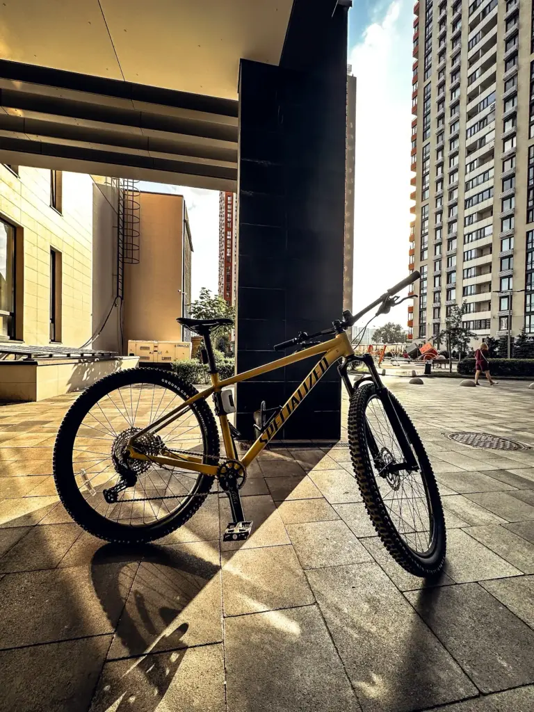 Yellow Specialized mountain bike leaning in sunlit urban plaza with high-rise apartments and long shadows