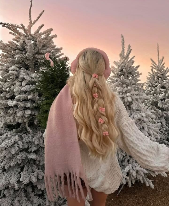 i l u v e Woman in winter attire with pink earmuffs and scarf, standing among snow-covered trees at sunrise, with braided hair adorned with bows. | Sky Rye Design Woman in winter attire with pink earmuffs and scarf, standing among snow-covered trees at sunrise, with braided hair adorned with bows. Winter Photoshoot