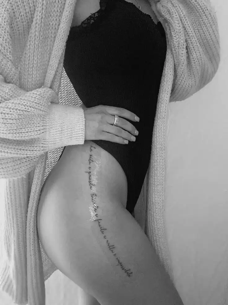 Woman in black bodysuit and cardigan showing side tattoo, hand on hip, monochrome elegance.